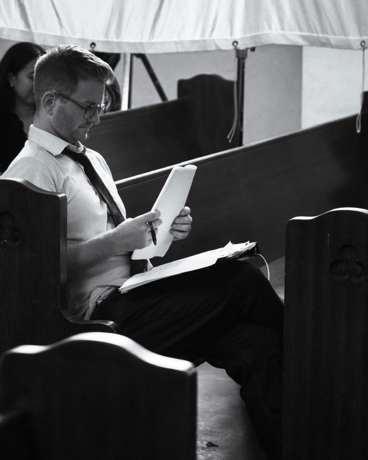 Patrick Westwater reading script pages in a church pew on the set of Holy Water